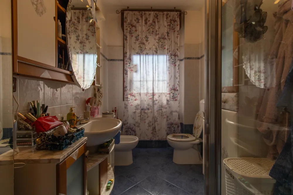 Bagno con lavabo, sanitari e finestra con tenda a fiori