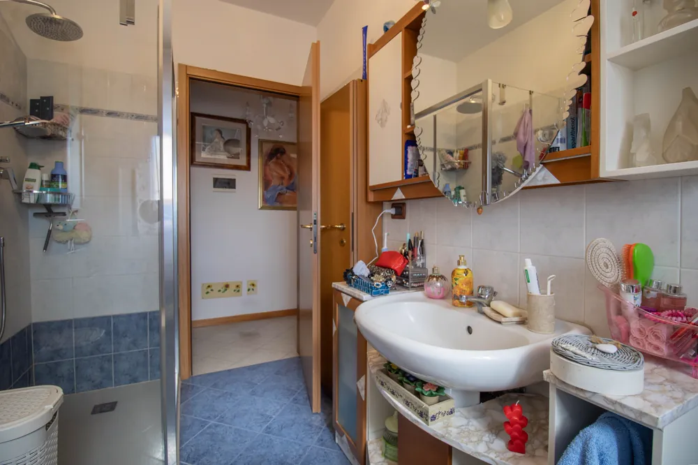 Bagno con box doccia e lavabo, porta aperta sul corridoio